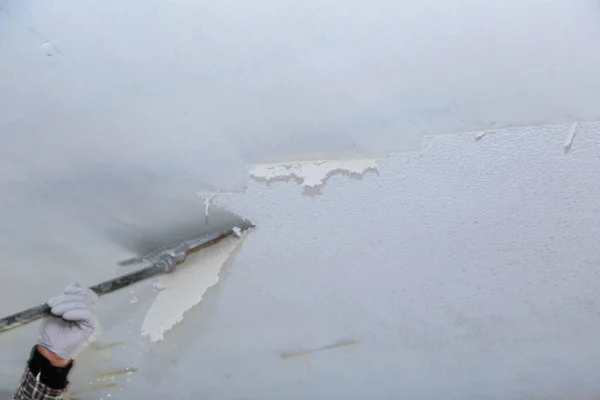 A person scraping the textured surface from a popcorn ceiling.