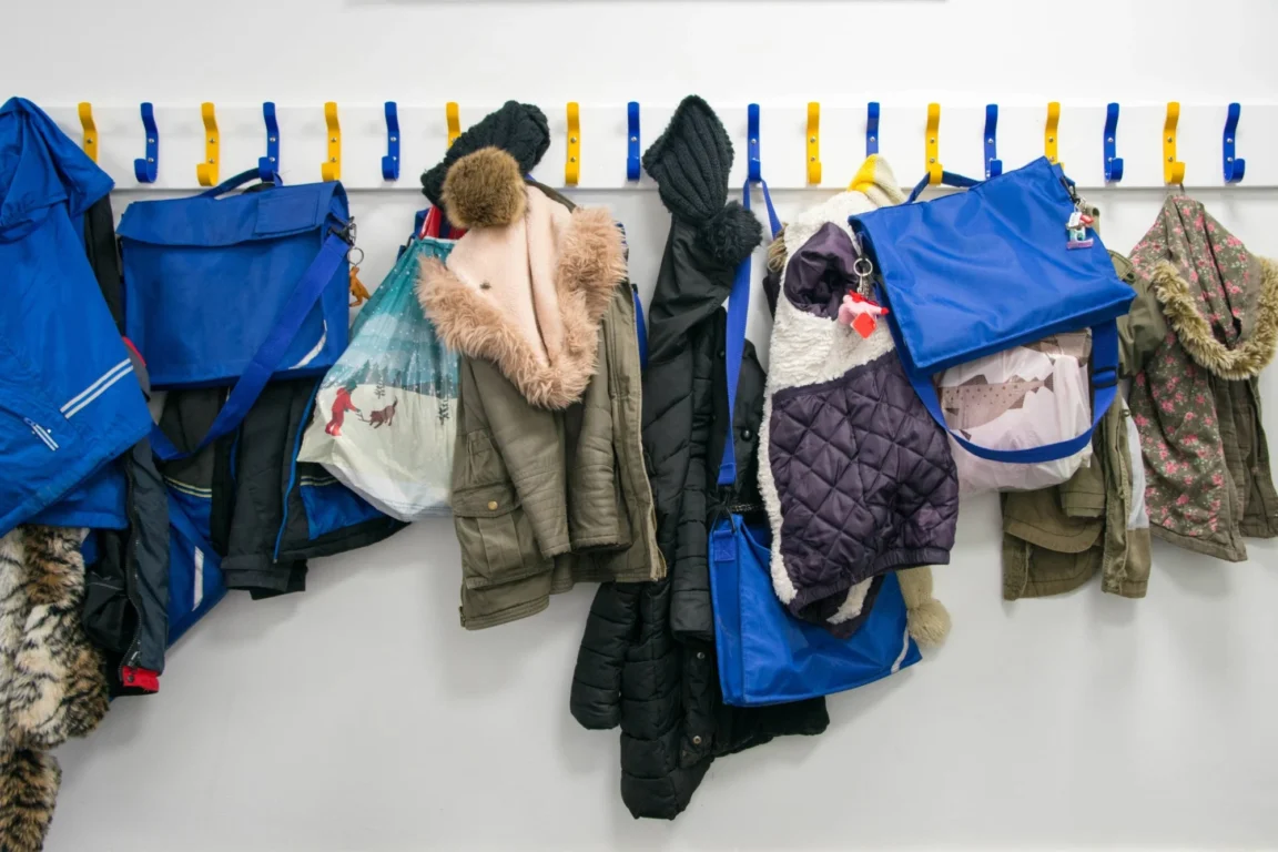 A primary school cloakroom with coats and book bags hanging on yellow and blue hooks.