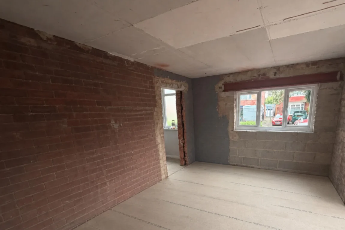 Empty garage interior before asbestos removal, showing bare brick walls and a ceiling made of asbestos insulating board.