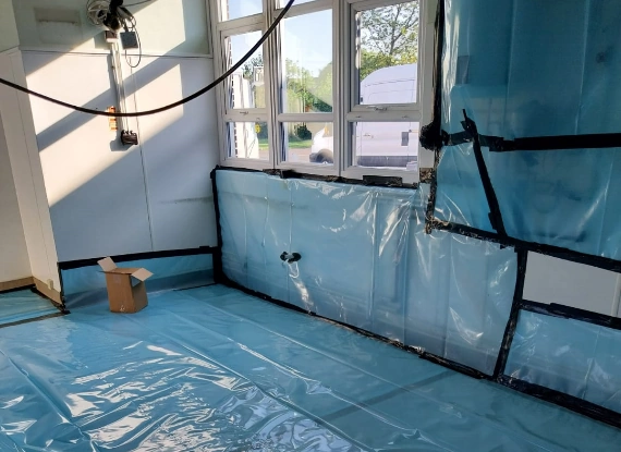 A room featuring a blue tarp spread across the floor, creating a protective surface for asbestos removal.