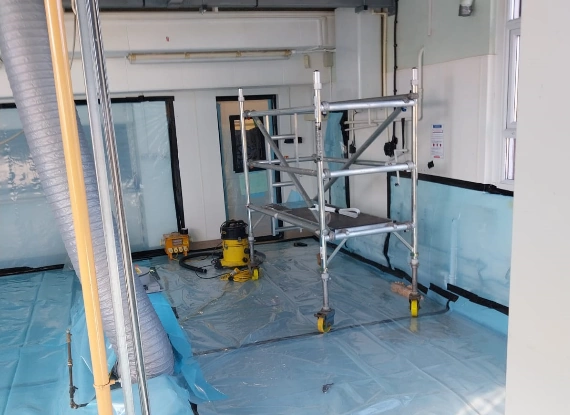 A room featuring a blue tarp spread across the floor and a ladder positioned against the wall.