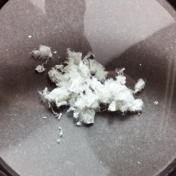 White, fluffy asbestos fibres viewed through a magnifying glass, emphasising their dangerous, loose form.