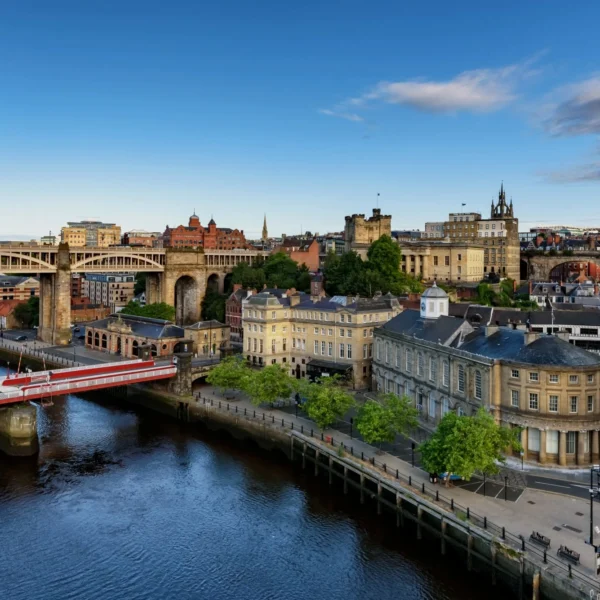 Elevated view of the Newcastle upon Tyne quayside, featuring historic architecture, the High Level Bridge, and the Swing Bridge over the River Tyne under a clear blue sky.