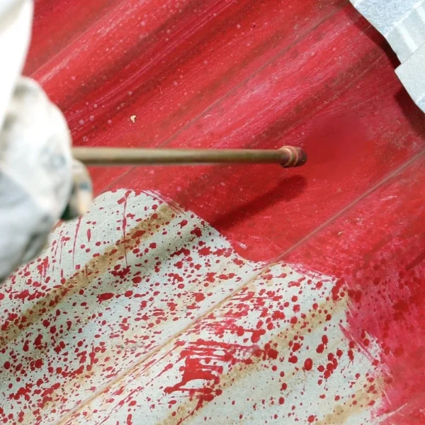 A red coating being applied to a corrugated metal roof.